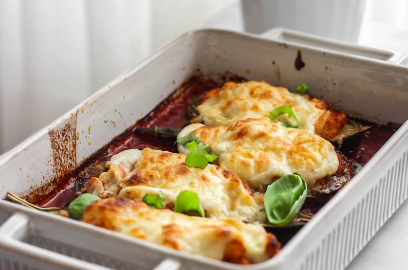 Appetizing baked eggplant parmesan topped with cheese and basil leaves in a ceramic dish.