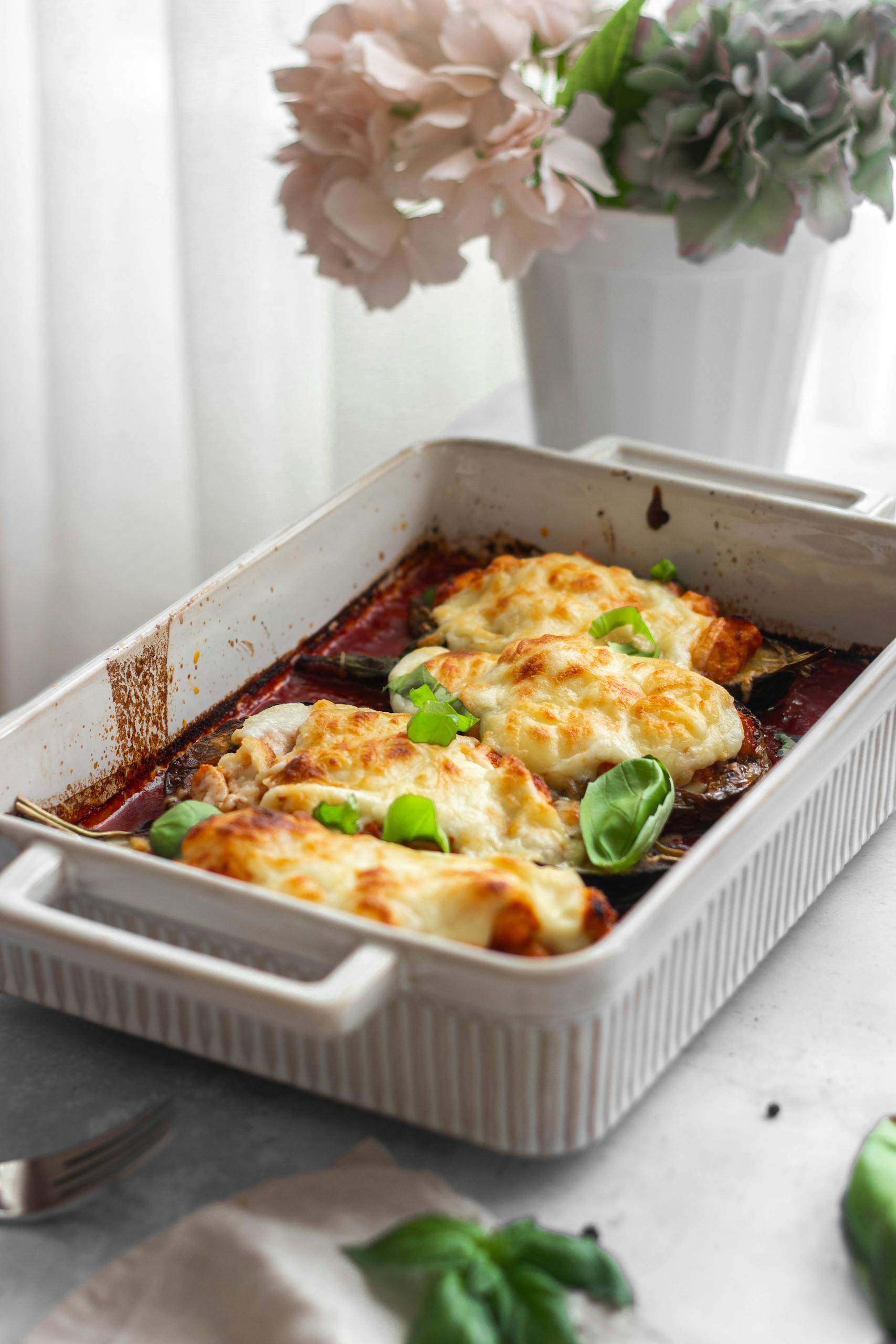 Appetizing baked eggplant parmesan topped with cheese and basil leaves in a ceramic dish.