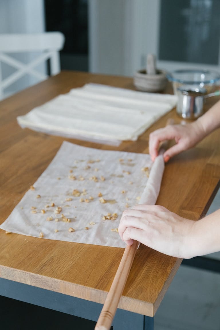 Hands preparing traditional Turkish baklava with phyllo dough on a wooden kitchen counter.