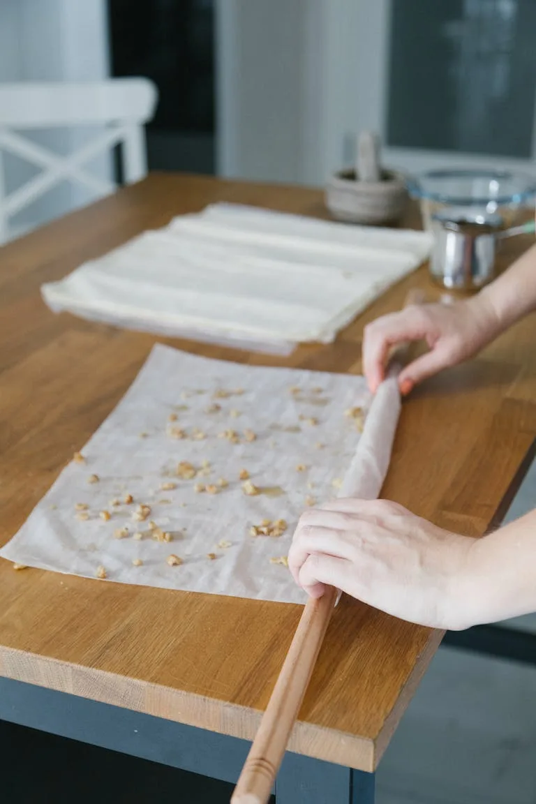 Hands preparing traditional Turkish baklava with phyllo dough on a wooden kitchen counter.