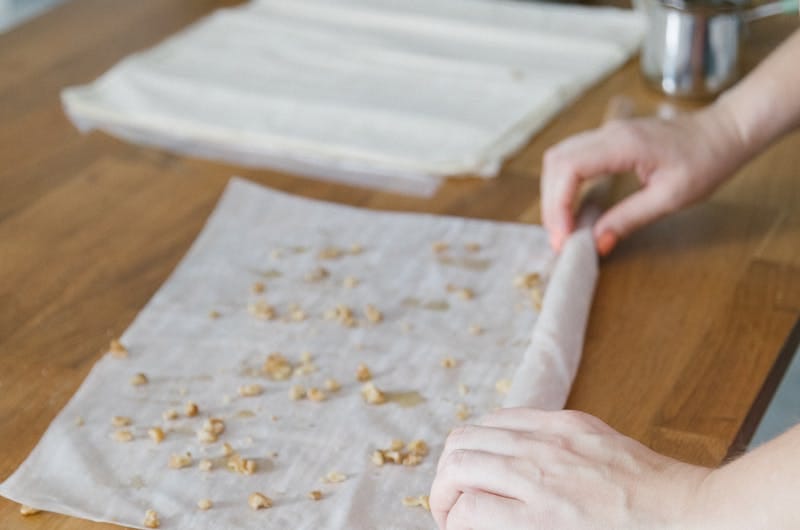 Hands preparing traditional Turkish baklava with phyllo dough on a wooden kitchen counter.