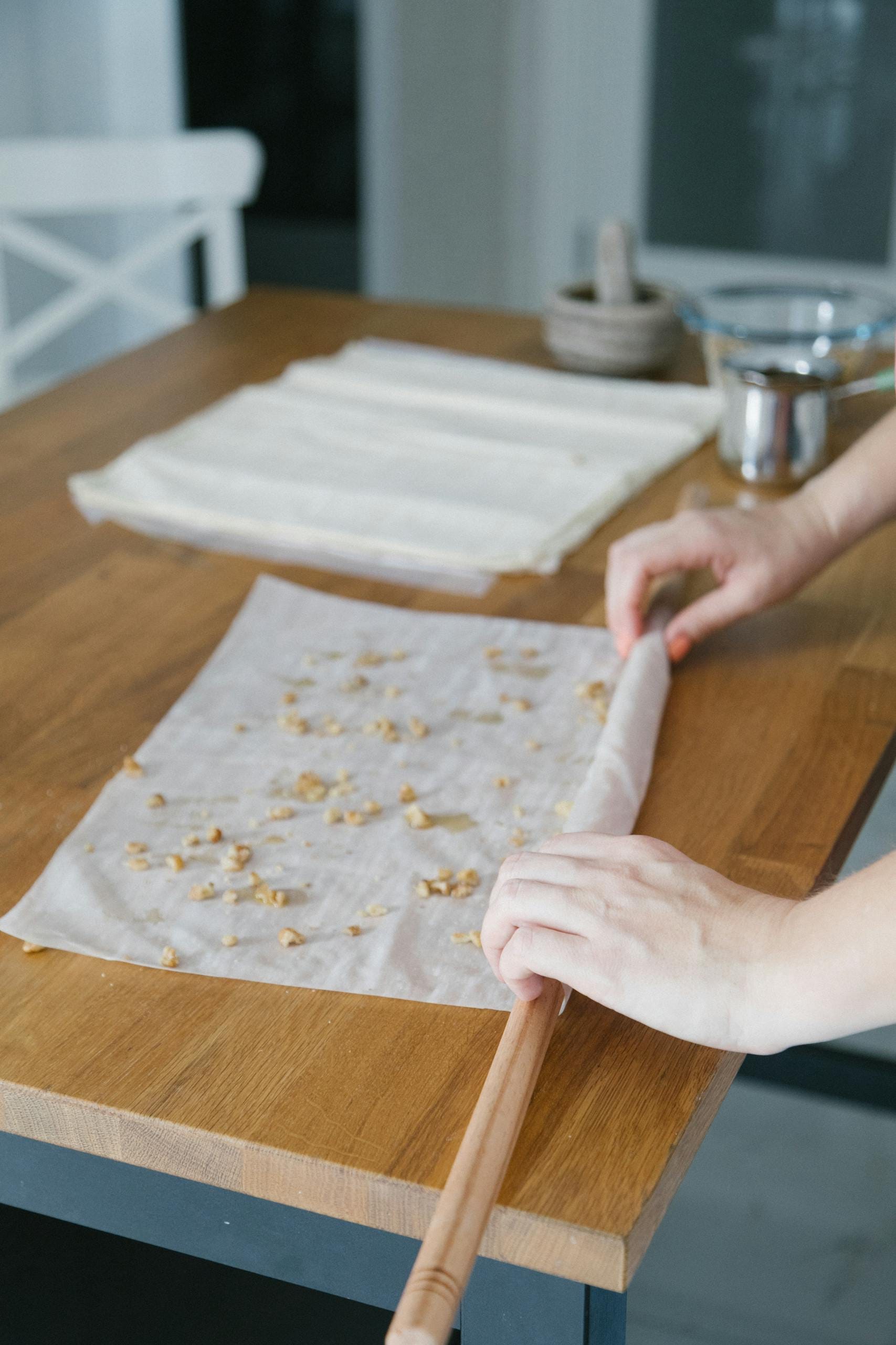 Hands preparing traditional Turkish baklava with phyllo dough on a wooden kitchen counter.