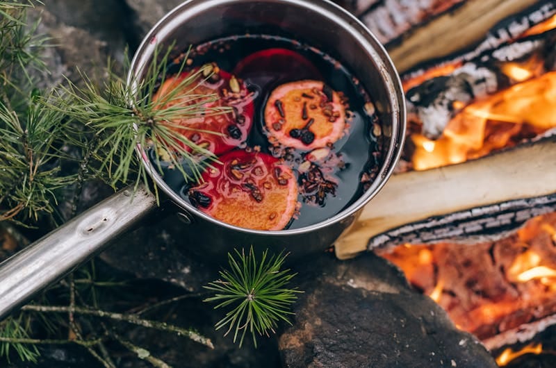 A warm pot of mulled wine with oranges by a campfire, perfect for a cozy outdoor experience.