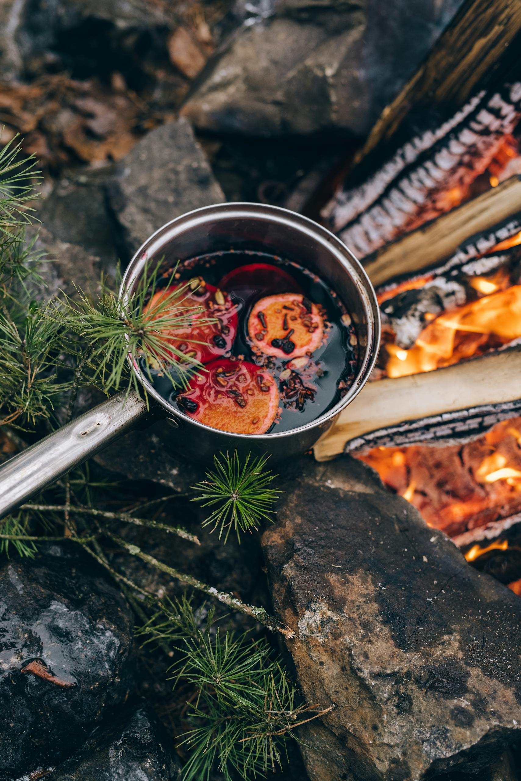 A warm pot of mulled wine with oranges by a campfire, perfect for a cozy outdoor experience.